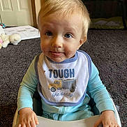 Ryan is registered to the contest to win money with this photo: toddler, child, baby, bib, high_chair, smiling, face, indoor, carpet, toy, clothing, hand, expression, blonde_hair, sitting, cute, messy_face, person, young_child, playful