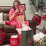 Holly joined the competition — help win amazing prizes! person, pajamas, gift, gift_bags, christmas, holiday_decor, couch, dog_bed, tissue_paper, plant, ornament, red, brown, white, carpet, smiling, celebration, indoor, festive, relaxing