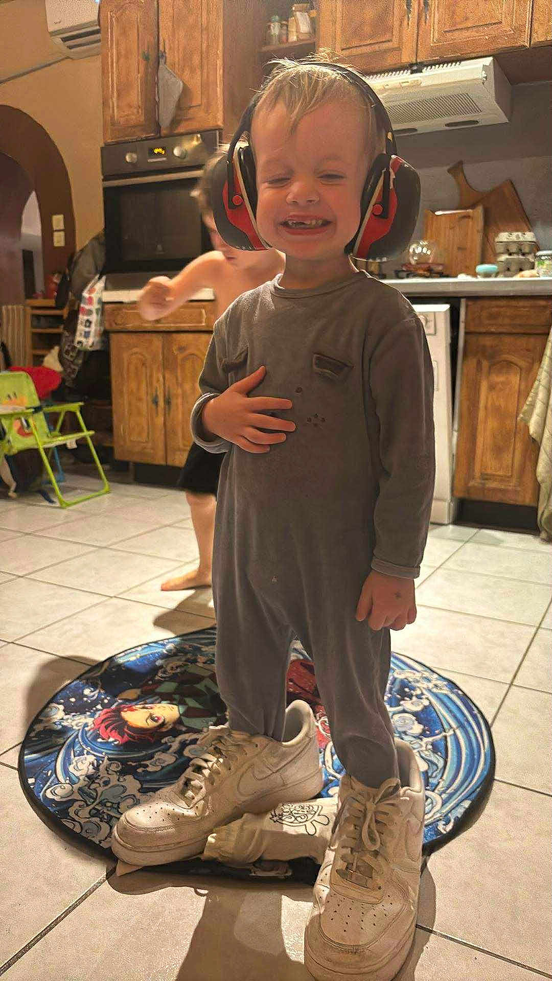 Stanley a rejoint le concours — aidez-le/la à gagner de superbes lots ! child, toddler, sneakers, oversized_shoes, ear_protection, kitchen, floor, tile_floor, rug, playful, smiling, indoor, clothing, cabinet, appliance, person, happy, cute, headphones, barefoot_child