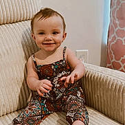 Elliana is registered to the contest to win money with this photo: baby, child, smiling, sitting, armchair, patterned_clothing, indoors, happy, cute, infant, face, portrait, furniture, feet, hand, wall, curtain, cozy, room, bright