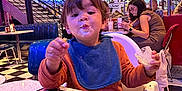 Marceau participe au concours pour gagner de l'argent avec cette photo : toddler, child, bib, food, messy_face, diner, retro, neon_lights, menu, table, chair, blue_chair, checkered_floor, woman, glasses, people, indoor, casual_clothing, eating, high_chair
