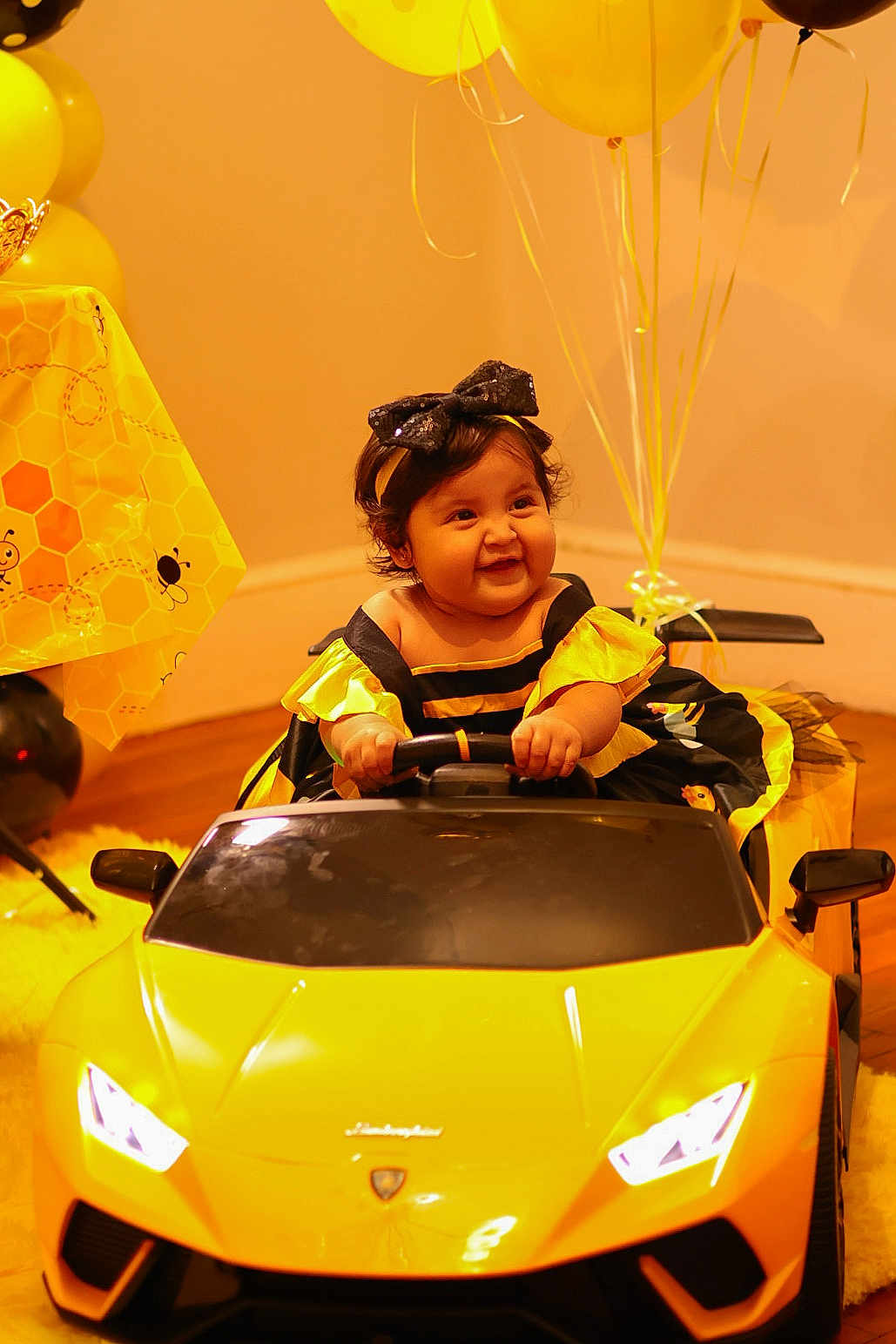 Kailani joined the competition — help win amazing prizes! baby, child, toy_car, yellow, balloons, party, smile, dress, headband, indoor, floor, celebration, happy, vehicle, hands, face, black, yellow_theme, cute, fun