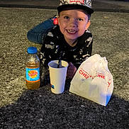 Pablo participe au concours pour gagner de l'argent avec cette photo : child, boy, smiling, cap, marvel, puma, jeans, bottle, drink, cup, straw, paper_bag, outdoor, night, pavement, happy, casual, food, person, evening