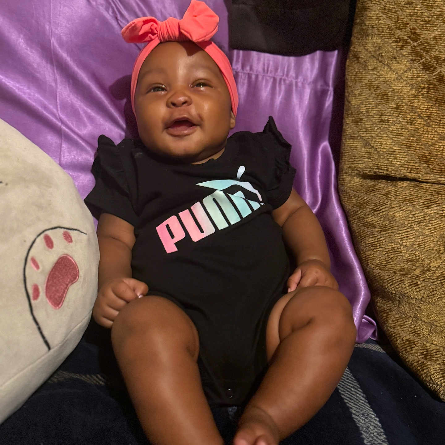 Aja is registered to the contest to win money with this photo: baby, black_onesie, brown_skin, child, clothing, cozy, cushion, cute, happy, headband, home, indoor, infant, pillow, pink, portrait, puma_logo, purple, sitting, smiling
