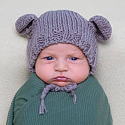 Richard is registered to the contest to win money with this photo: baby, infant, knitted_hat, bear_ears, blue_eyes, swaddle, green_clothing, chubby_cheeks, portrait, close_up, cute, serious_expression, soft_background, texture, headwear, child, newborn, indoors, warm_clothing, young_child