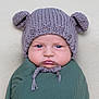 baby, infant, knitted_hat, bear_ears, blue_eyes, swaddle, green_clothing, chubby_cheeks, portrait, close_up, cute, serious_expression, soft_background, texture, headwear, child, newborn, indoors, warm_clothing, young_child