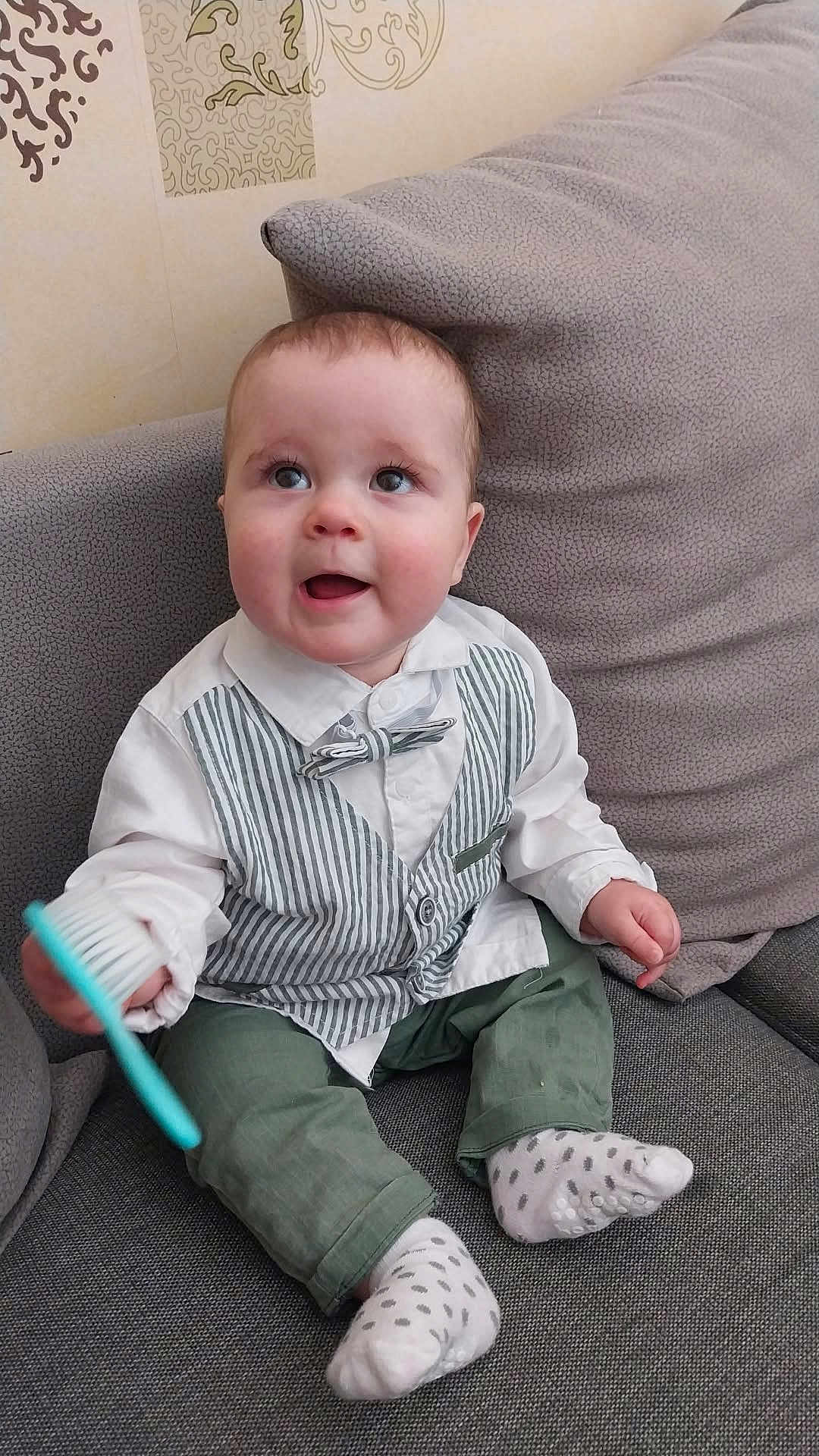 Arthur participe au concours pour gagner de l'argent avec cette photo : baby, child, toddler, couch, sofa, clothing, vest, bow_tie, green_pants, socks, brush, indoor, cute, smiling, happy, person, home, seated, face, expression