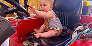 Arthur participe au concours pour gagner de l'argent avec cette photo : baby, child, curious, exploration, expression, farm_equipment, footwear_free, handle, indoor, person, red, rope, seat, short_sleeves, shorts, steering_wheel, toy_beads, tractor, vehicle, wooden_wall
