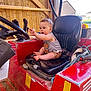 baby, child, curious, exploration, expression, farm_equipment, footwear_free, handle, indoor, person, red, rope, seat, short_sleeves, shorts, steering_wheel, toy_beads, tractor, vehicle, wooden_wall