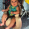 baby, child, infant, stroller, sitting, portrait, face, wide_eyed, looking_at_camera, colorful_clothing, romper, barefoot, feet, carpet, indoor, patterned_fabric, padded_seat, harness, wheelchair_like_stroller, photography