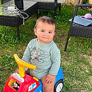 Carlos joined the competition — help win amazing prizes! baby, child, toddler, ride_on_toy, toy_car, outdoor, garden, grass, patio, furniture, chair, table, smiling, portrait, sitting, barefoot, clothing, greenery, backyard, playtime