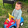 baby, child, toddler, sitting, toy_car, ride_on_toy, outdoor, garden, grass, backyard, patio, furniture, table, chair, speaker, clothing, long_sleeves, barefoot, serious_expression, portrait