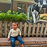 Carlos joined the competition — help win amazing prizes! baby, child, toddler, smiling, sitting, outdoor, cow_statue, animal_statue, garden, picket_fence, brick_building, landscaping, trees, plants, sunlight, portrait, baby_clothing, jeans, sandals, family_photo
