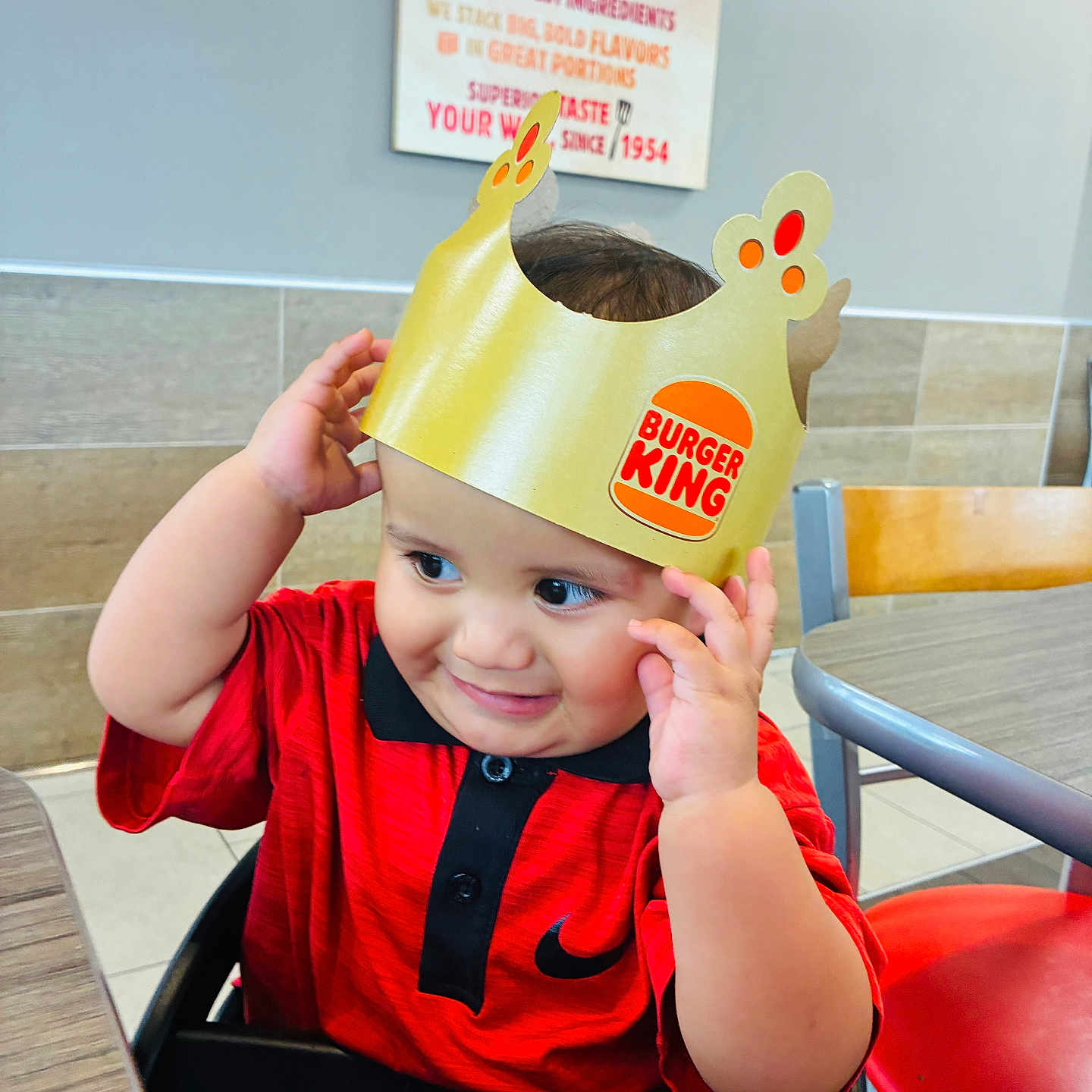 Carlos joined the competition — help win amazing prizes! baby, child, infant, portrait, smiling, happy, restaurant, fast_food, burger_king, crown, paper_hat, red_shirt, high_chair, sitting, indoor, table, chair, background_sign, hands, playful