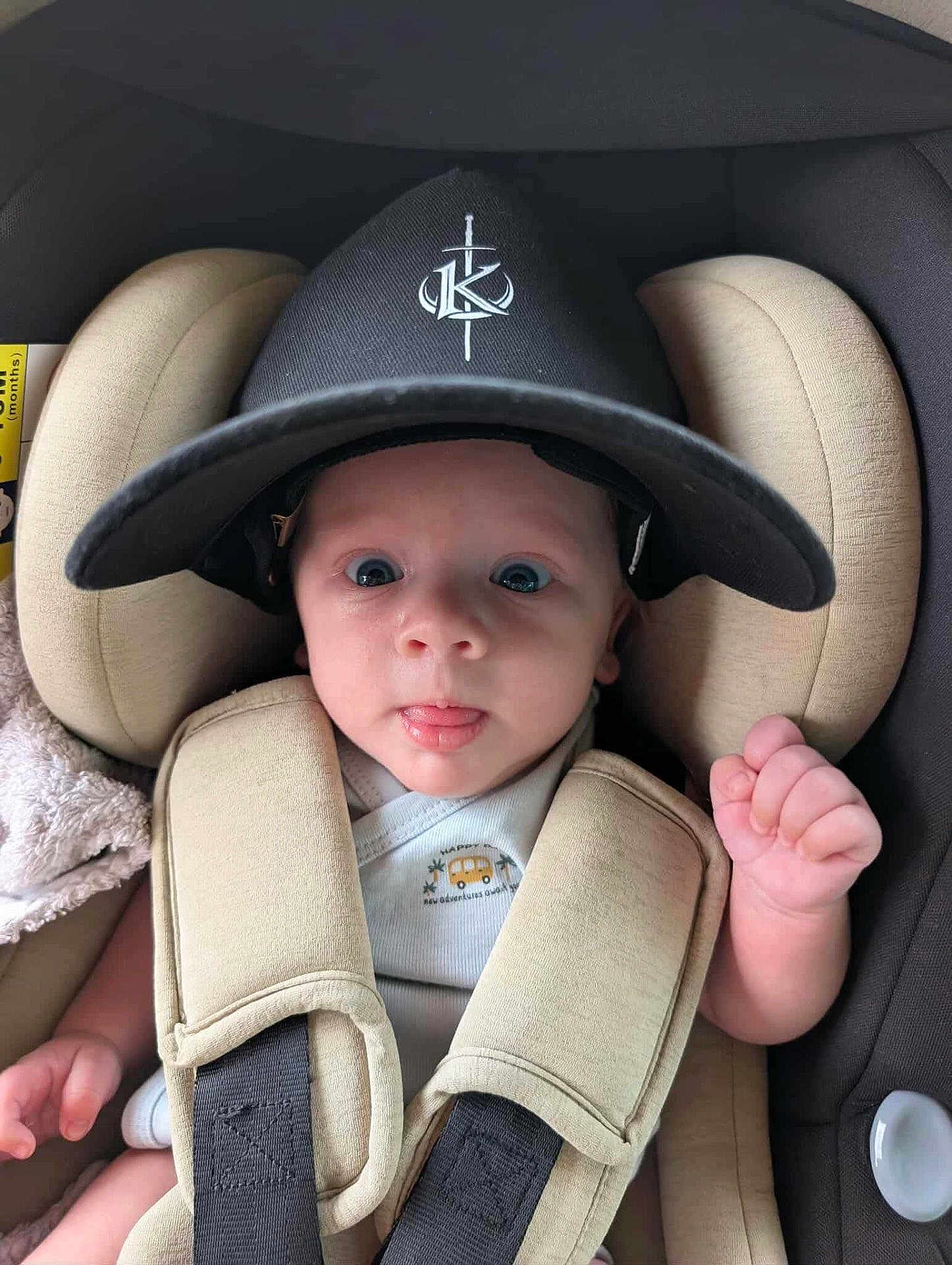 Arthur participe au concours pour gagner de l'argent avec cette photo : baby, infant, car_seat, cap, hat, straps, cute, tongue_out, wide_eyes, child, seat_belt, clothing, person, young, adorable, indoor, expression, headwear, padded, safety