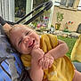 Arthur participe au concours pour gagner de l'argent avec cette photo : baby, child, smiling, yellow_bib, hand, face, outdoor, garden, potted_plants, pinwheel, window, reflection, person, happy, grass, clothing, socks, home, daylight, seated