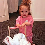 Emi joined the competition — help win amazing prizes! toddler, child, smiling, pink_clothing, toy_stroller, blanket, indoor, carpet, door, baby_gate, hair_updo, person, happy, playful, cute, young_child, home, furniture, floor, wall