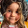 Yléana a rejoint le concours — aidez-le/la à gagner de superbes lots ! child, face, wig, hair, smile, portrait, indoor, striped_shirt, brown_eyes, curly_hair, close_up, person, cute, young_child, expression, warm_lighting, casual_clothing, background, colorful, headwear
