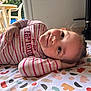toddler, child, smiling, striped_shirt, patterned_blanket, indoor, floor_tiles, hand_on_head, playful, relaxed_pose, colorful, person, young_child, casual, home, happy, face, portrait, clothing, nail_polish