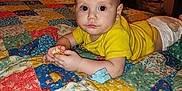 Lucas is registered to the contest to win money with this photo: baby, child, yellow_shirt, diaper, patchwork_quilt, bed, indoor, toy, puzzle_piece, fan, furniture, room, person, face, hand, curious, light, food, candid, portrait