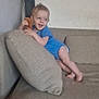 toddler, child, blue_onesie, couch, cushion, comb, happy, smiling, indoor, living_room, bare_wall, barefoot, hair_tuft, playful, furniture, person, cute, small_child, home, relaxed