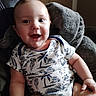 Silas is registered to the contest to win money with this photo: baby, infant, child, smiling, happy, portrait, sitting, chair, cushion, indoor, home, face, eyes, mouth, short_hair, onesie, patterned_clothing, hands, legs, cozy