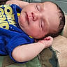 baby, newborn, sleeping, infant, blue_shirt, yellow_text, hand, face, closed_eyes, skin, hair, camo_fabric, clothing, resting, peaceful, close_up, portrait, person, indoors, soft_lighting