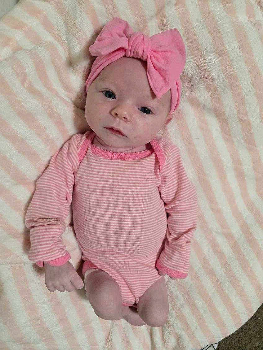 Reagan Tigerlily is registered to the contest to win money with this photo: baby, infant, pink, headband, bow, striped_onesie, blanket, striped_blanket, lying_down, cute, soft_texture, child, newborn, portrait, indoors, skin, face, hands, legs, clothing