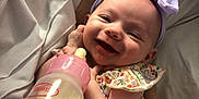Reagan Tigerlily is registered to the contest to win money with this photo: baby, smiling, headband, bottle, feeding, arms, person, watch, clothing, floral_pattern, happy, infant, cute, hand, nurturing, closeup, indoor, skin, face, pink