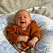 Dulcie-Mae is registered to the contest to win money with this photo: baby, infant, smile, happy, face, portrait, clothing, orange, cushion, pattern, fabric, bed, comfort, child, young, cute, skin, person, hands, sitting