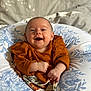 baby, infant, smile, happy, face, portrait, clothing, orange, cushion, pattern, fabric, bed, comfort, child, young, cute, skin, person, hands, sitting