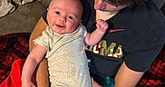 August is registered to the contest to win money with this photo: baby, child, couch, blanket, red_shorts, grey_onesie, smile, happy, indoor, person, holding, affection, family, hair, face, arm, seated, clothing, comfort, home