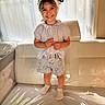child, girl, smile, headband, shorts, couch, indoor, window, light, happy, standing, clothing, plastic_cover, sock, person, portrait, cute, home, furniture, casual