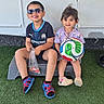 child, children, boy, girl, sunglasses, soccer_ball, outdoor, grass, step, smiling, casual_clothing, sporty, happy, toy, playing, summer, daylight, portrait, friends, cute