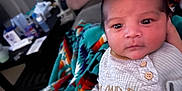 Dakota is registered to the contest to win money with this photo: baby, infant, onesie, blanket, colorful, patterned_blanket, face, person, indoor, couch, hand, clothing, cute, newborn, portrait, expression, eyes, soft_lighting, home, cozy