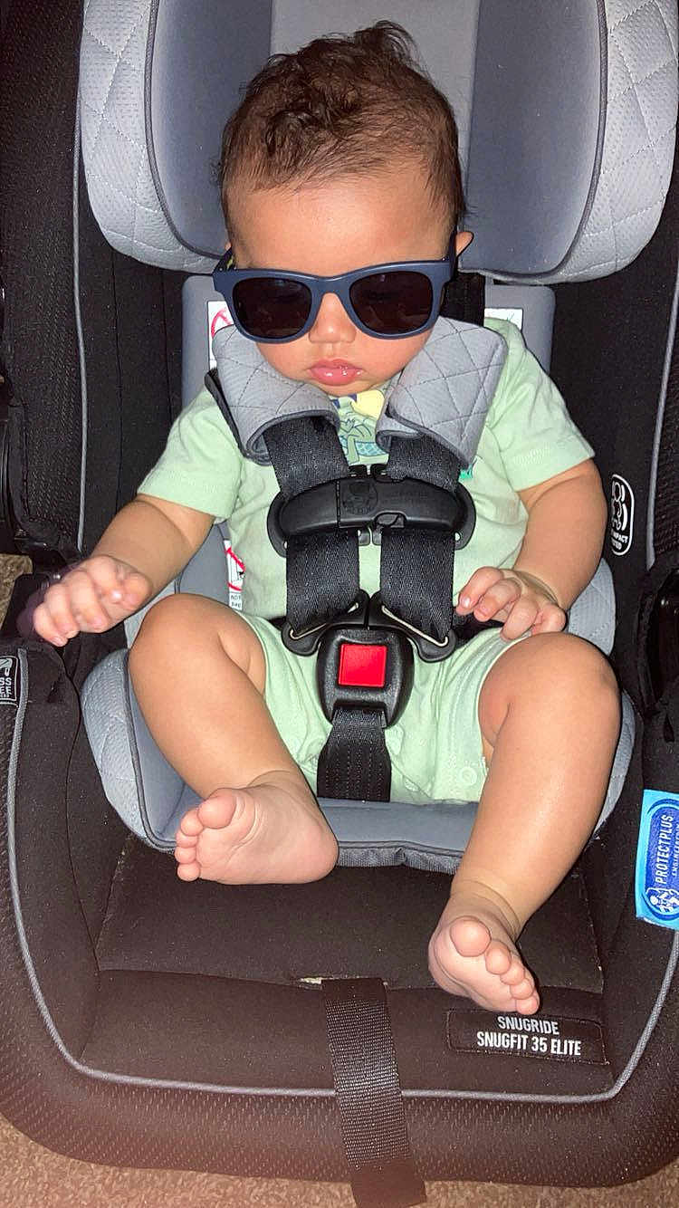 Julian is registered to the contest to win money with this photo: baby, sunglasses, car_seat, child, infant, safety_harness, cute, clothing, foot, hand, seat, indoor, person, toddler, head, eyewear, resting, infant_clothing, baby_seat, strap