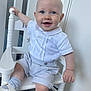 baby, child, smiling, blue_eyes, white_shirt, checkered_shorts, sitting, chair, indoor, wooden_chair, happy, cute, footwear, sock, hand, face, portrait, infant, clothing, floor