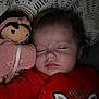 baby, sleeping, doll, red_clothing, reindeer, blanket, bed, face, child, cute, indoors, peaceful, soft_toy, portrait, infant, resting, young_child, cozy, closeup, head