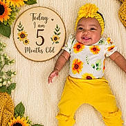 Kaylee joined the competition — help win amazing prizes! age_marker, baby, blanket, bright_colors, clothing, cute, decor, flower, greenery, happy, headband, infant, lying_down, portrait, smiling, socks, soft_texture, sunflower, wooden_plaque, yellow