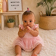Kaylee joined the competition — help win amazing prizes! baby, infant, girl, pink_dress, sitting, carpet, indoor, plant, milestone, sign, decor, cute, portrait, child, young, expression, hands, hair_clip, floor, home