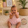 baby, infant, child, pink_dress, sitting, smiling, fingers_in_mouth, carpet, fairy_lights, sign, flowers, vase, plant, basket, table, indoor, portrait, cute, decor, six_months