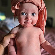 Isabella is registered to the contest to win money with this photo: baby, infant, child, portrait, close_up, wide_eyes, smiling, head_wrap, pink, towel, bare_chested, held, adult_hand, indoor, bedroom, soft_lighting, bokeh, sitting, human_face, photography