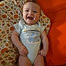 Isabella is registered to the contest to win money with this photo: baby, infant, child, smiling, happy, portrait, sitting, indoors, blanket, cushion, orange, pumpkin_pattern, onesie, clothing, face, eyes, mouth, baby_bed, soft_furnishings, photography