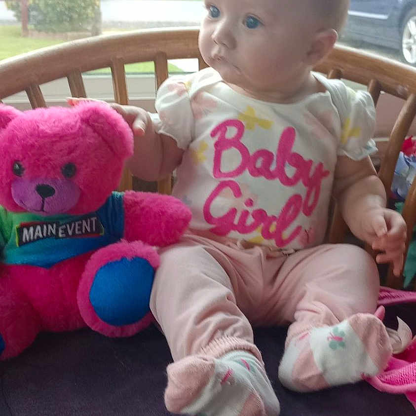Isabella joined the competition — help win amazing prizes! baby, child, infant, sitting, portrait, face, eyes, looking_away, teddy_bear, stuffed_toy, pink, baby_clothing, onesie, shoes, chair, cushion, indoor, window, residential_background, photography