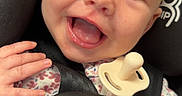 Kinsley is registered to the contest to win money with this photo: baby, smiling, car_seat, pacifier, child, happy, face, hand, clothing, infant, seatbelt, closeup, cute, portrait, safety, floral_pattern, young_child, indoors, person, joy