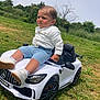 toddler, child, toy_car, outdoor, grass, white_shirt, blue_shorts, miniature_car, amg, greenery, summer, footwear, casual_clothing, vehicle, playing, young_child, nature, daylight, expression, sitting