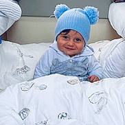 Harsëne a rejoint le concours — aidez-le/la à gagner de superbes lots ! toddler, child, blue_hat, pom_poms, smile, blanket, feather_print, bed, cozy, indoor, cute, clothing, person, portrait, face, warm, happy, soft, young, resting
