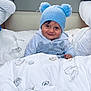 toddler, child, blue_hat, pom_poms, smile, blanket, feather_print, bed, cozy, indoor, cute, clothing, person, portrait, face, warm, happy, soft, young, resting