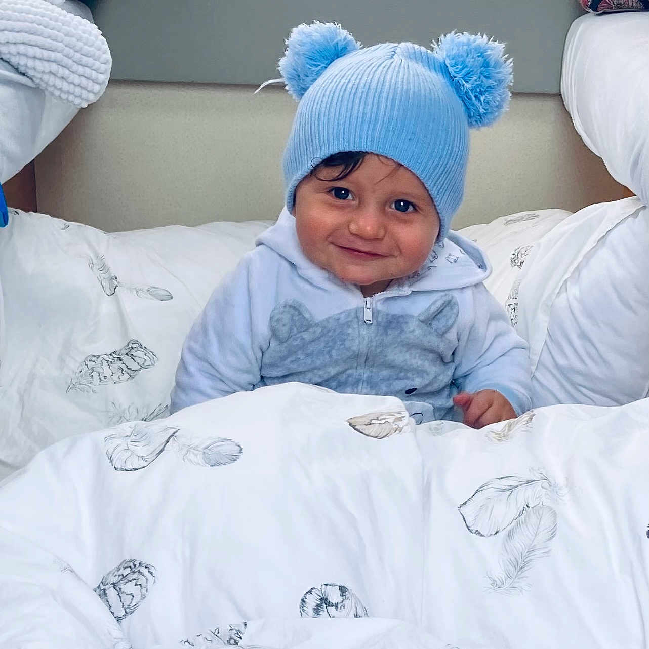 Harsëne a rejoint le concours — aidez-le/la à gagner de superbes lots ! bed, blanket, blue_hat, child, clothing, cozy, cute, face, feather_print, happy, indoor, person, pom_poms, portrait, resting, smile, soft, toddler, warm, young