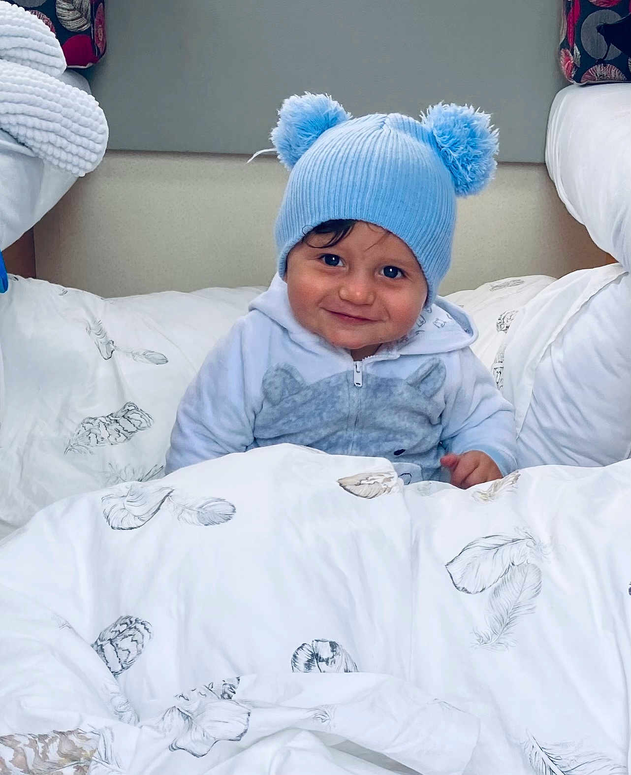 Harsëne a rejoint le concours — aidez-le/la à gagner de superbes lots ! toddler, child, blue_hat, pom_poms, smile, blanket, feather_print, bed, cozy, indoor, cute, clothing, person, portrait, face, warm, happy, soft, young, resting